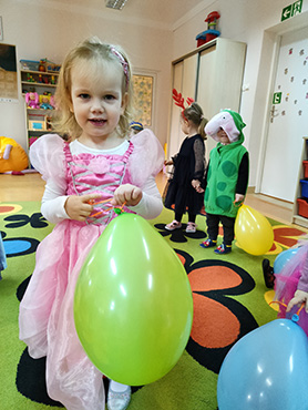 Zdjęcie przedstawia uśmiechniętą dziewczynkę z balonem.