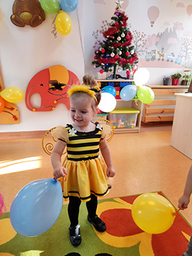 Na zdjęciu widać uśmiechniętą dziewczynkę w stroju pszczółki, która bawi się balonem.