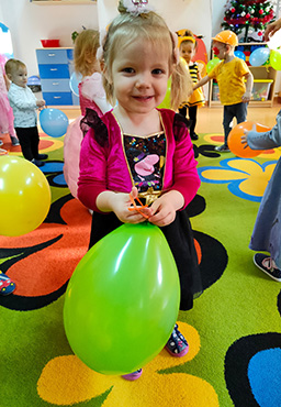 Na zdjęciu widać uśmiechniętą dziewczynkę, która bawi się balonem.