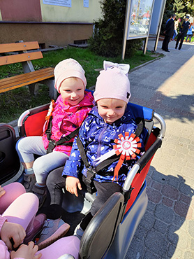 Na zdjęciu widać uśmiechnięte dzieci w wózku przy Urzędzie Miasta Hajnówka.