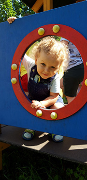 Na zdjęciu widać uśmiechniętego chłopca, który zagląda przez okienko na placu zabaw.