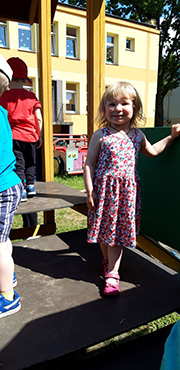 Zdjęcie przedstawia uśmiechniętą  dziewczynkę, na placu zabaw.