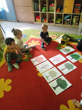 Dzieci siedzą na dywanie i oglądają plansze drzewa w różnych porach roku