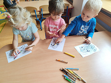 Na zdjęciu widać troje dzieci przy stoliku, które kolorują obrazek.