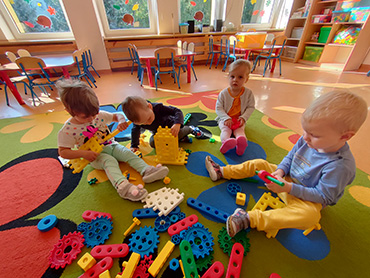 Na trzecim zdjęciu widać czworo dzieci, bawiące się na dywanie.