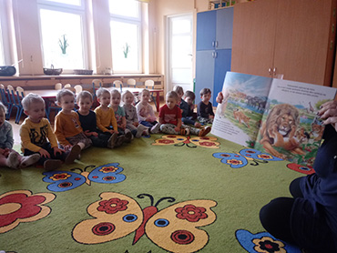 Pani pokazuje dzieciom książkę, na której jest stado lwów.