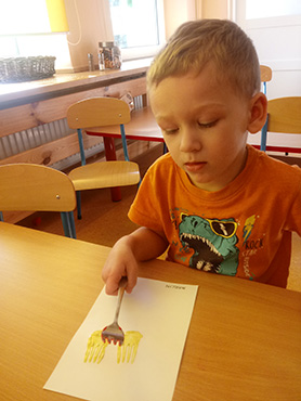 Chłopczyk odbija widelec umoczony w farbie na kartce papieru