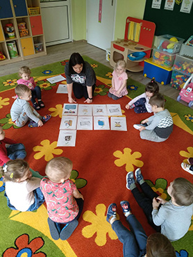 dzieci siedzą na dywanie w kole, Pani przedstawia za pomocą ilustracji zasady korzystania z książek