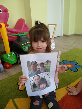 Dziewczynka trzyma zdjęcie, na którym jest z mamą i tatą