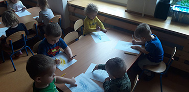 Na zdjęciu widać dzieci siedzące przy stolikach, które kolorują swoje obrazki.