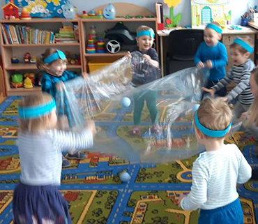 Dzieci bawiące się folią imitującą fale na morzu.