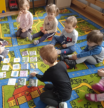 Dzieci siedzą na dywanie i oglądają na ilustracjach pierwsze oznaki wiosny i marcowej pogody