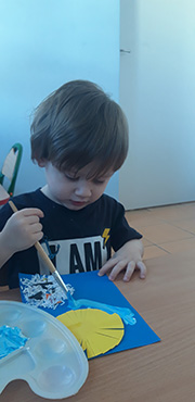 Zdjęcie przedstawia chłopca, który maluje farbami.