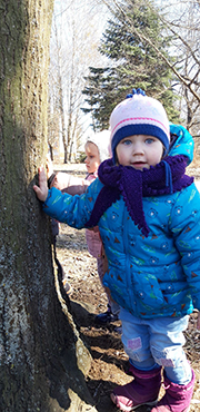 Zdjęcie przedstawia dziewczynkę, która bada jaką strukturę ma kora drzewa.