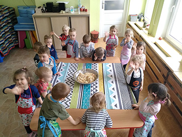 Dzieci stoją wokół stolika, na którym stoi przygotowana już sałatka warzywna