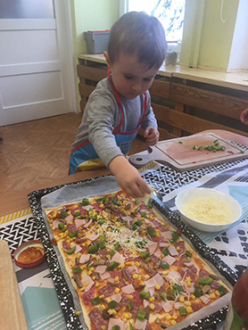 chłopczyk posypuje serem żółtym pizzę