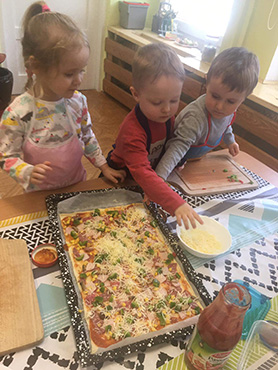 dwóch chłopców i dziewczynka sypią ser żółty na tygrysią pizzę