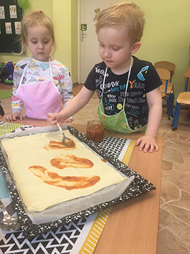 chłopczyk smaruje passatą pomidorową spód tygrysiej pizzy, obok stoi dziewczynka