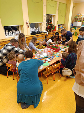 Rodzice razem z dziećmi przy stole wykonują ozdoby bożonarodzeniowe